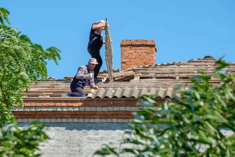 Men remove old sheets of roofing slate from the roof of a building. Stock Photos