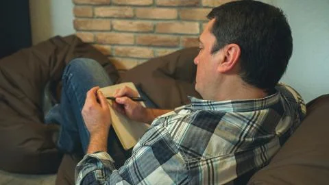 Men rest on the sofa and make notes in the notebook Stock Photos