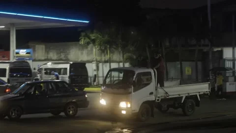 Men riding in back of work truck by gas station in Nicaragua, night time Stock Footage 209338241
