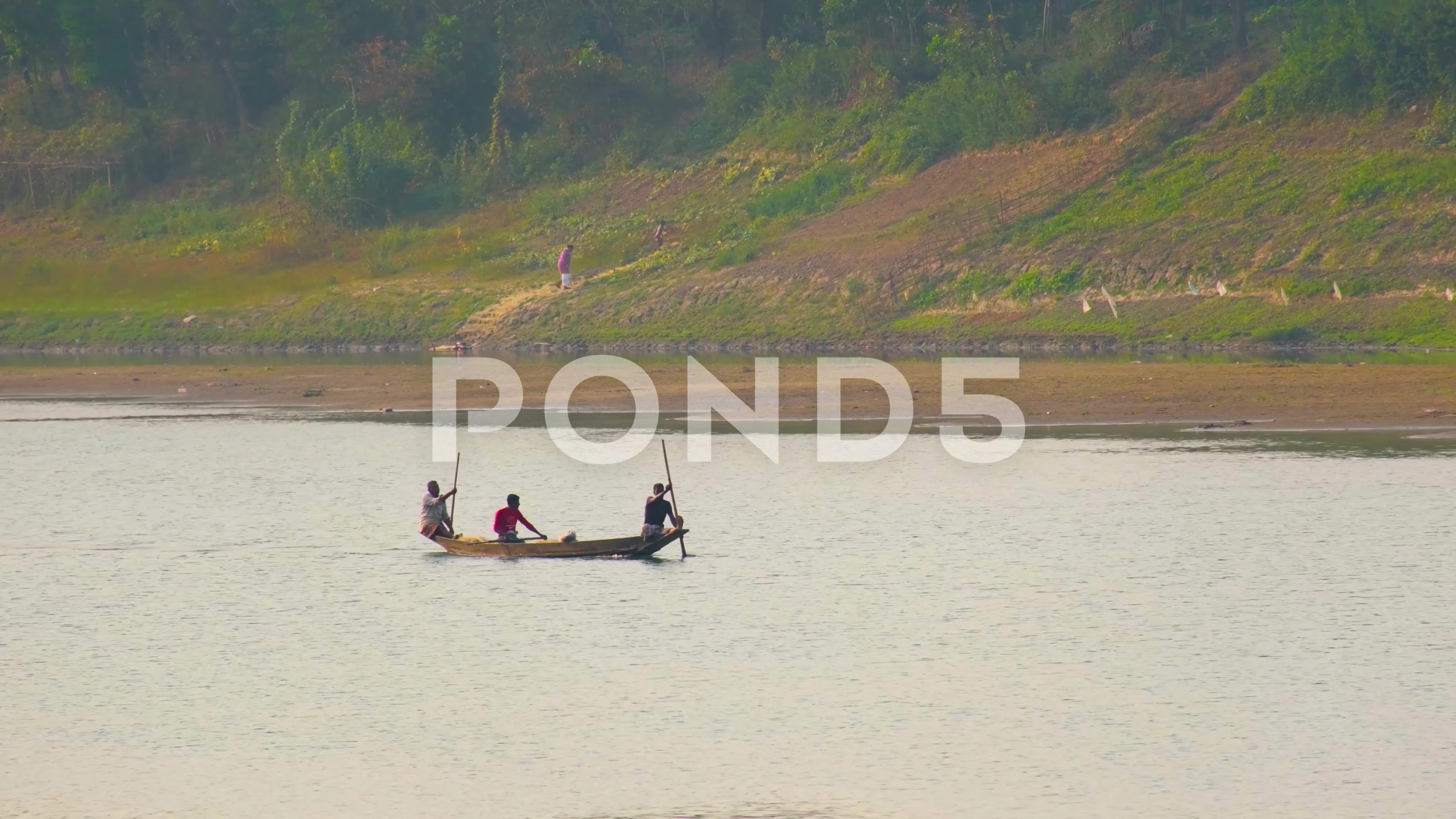 Men row down river using long paddles in canoe across calm water by