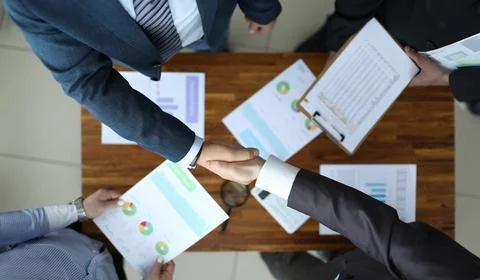 Men shake hands over the table with reports. Stock Photos