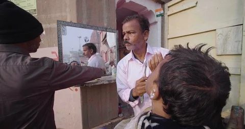 Men shaving beard of his customer in street saloon for cheap, Varanasi Stock Footage 125229701