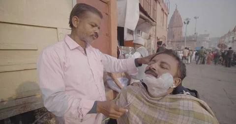 Men shaving beard of his customer in street saloon for cheap, Varanasi Stock Footage 125229811