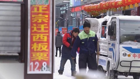 Men shifting snow using truck and people walk by in snowy China, Shenyang 스톡 동영상 84385298