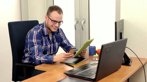 Men, siting behing his desk and alternately using tablet and smartphone, Stock-Footage 49058467