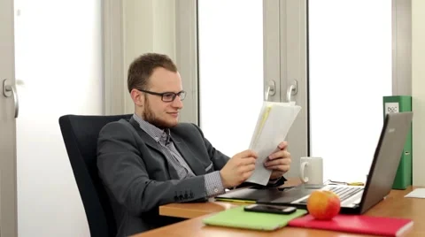 Men sitting behind the desk and in the same time he is  reading notes. (44) Video stock 49340265