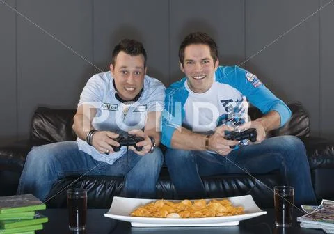 Men sitting on couch and playing video game, smiling Stock Photos