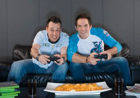 Men sitting on couch and playing video game, smiling Stock Photos