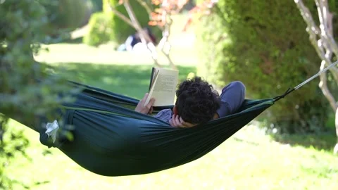 A Men sleeping in a camping hammock and reading a book Stock Footage 228827932