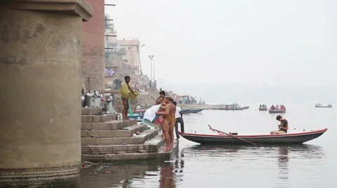 Men standing on dock of Ganges after bath, with man in boat on river. Stock Footage 50343137