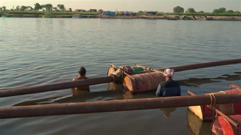 Men submerged in river water working around floating metal pipes and drums Stock Footage 341109820