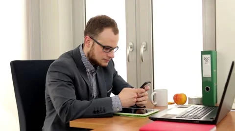 Men in suit sitting in the office behind his desk and  using smartphone. Video stock 49338520