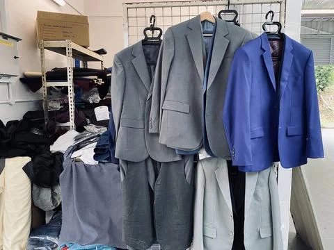 Men suits jacket hanging on the rack factory tailor Stock Photos