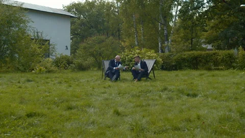 Men in suits sit in courtyard with papers and chat. Stock Footage 118377100