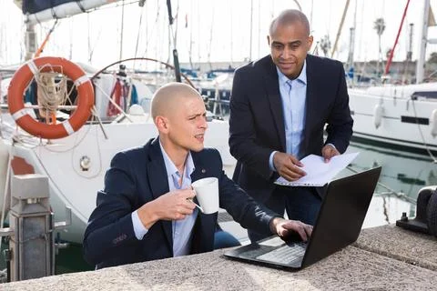 Men in suits verifying documentation on a laptop in the seaport Stock Photos