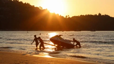 Men at sunset pull hydro cycle out of the water on a sandy beach.  Summer vacati Stock Footage 119258098