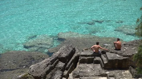 Men talking on rocks by the beach Stock Footage 128348832