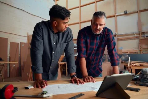 Men talking while working by table with digital tablet and paper in woodworking Stock Photos