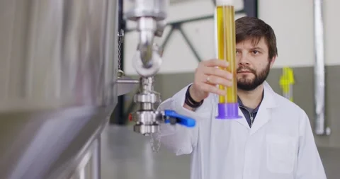 Men testing quality of fresh beer in a brewery. Brewer dressed in lab coat Stock Footage 148391298
