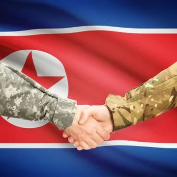 Men in uniform shaking hands with flag on background - North Korea Foto stock