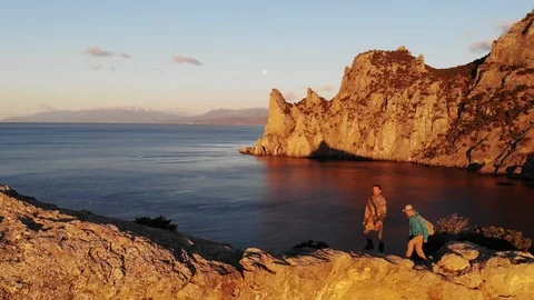 Men walk on cliff crest top above sea under evening sky Video stock 103835990