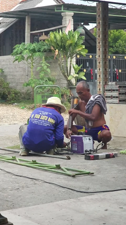 Men working on metal frame outdoors with one welding and another smoking Stock Footage 340079543