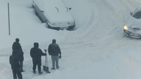 Men working together to free car stuck in deep snow during winter storm, street Stock Footage 344864989