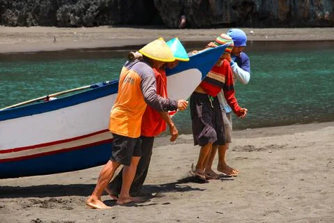 Men working together pulling traditional boat out of water Stock Photos