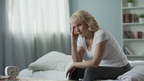 Menopause. Adult female sitting on bed and suffering from migraine, health Stock Footage