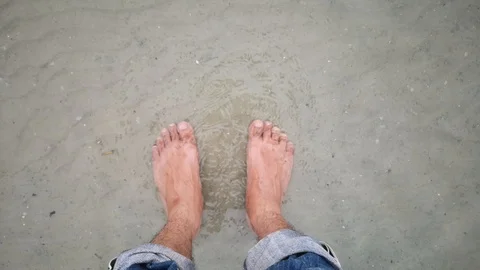 Men's feet on sandy beach into sea wave, point of view. Stock Footage 99821153