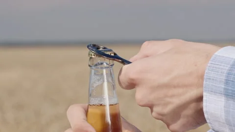 Men's hand opens a bottle of beer against the background of the field where Stock Footage 136356879