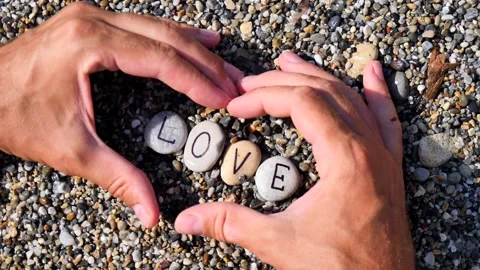 Men's hands folded in shape of a heart hold sea stones with word love written Stock Footage 138751667