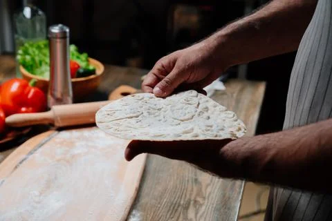 Men's hands hold a thin flatbread. Cooking pizza, noodles or pitta at home Stock Photos