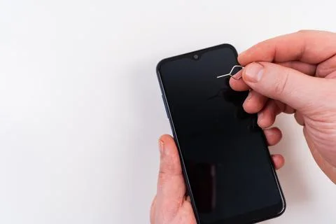 Men's hands insert a SIM card into a smartphone using a clip key Stock Photos