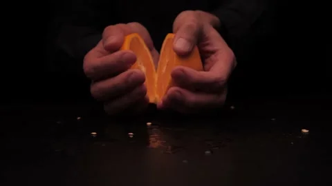 Men's hands offer to hold two parts of a yellow orange on a dark background Stock Footage 142863285