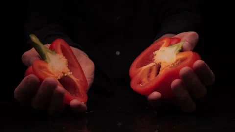 Men's hands offer to hold two pieces of red bell pepper on a dark background Stock Footage 142863572