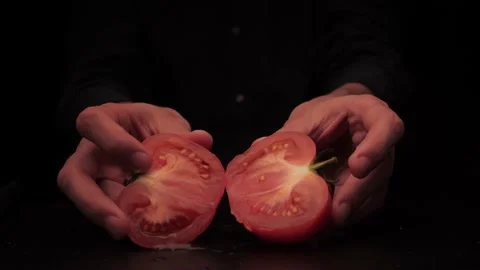 Men's hands offer to hold two parts of a tomato on a dark background Stock-Footage 142863950