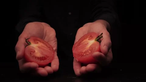 Men's hands offer to hold two parts of a tomato on a dark background Stock Footage 144370635