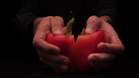 Men's hands offer to hold two pieces of red bell pepper on a dark background Stock-Footage 144370660
