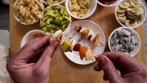 Mens hands string pieces of fresh fruit on a wooden skewer to make fruit kebabs 動画素材 330060151
