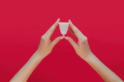 Menstrual cup in hands on red background. Alternative feminine hygiene produc Stock Photos