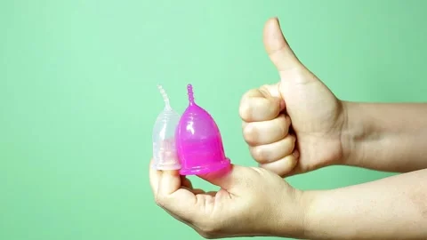 Menstrual cups of different colors on a woman's palm on a green background 스톡 동영상 160895057