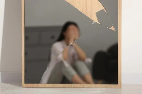 Mental problems. Blurred reflection of depressed woman in broken mirror indoo Stock Photos