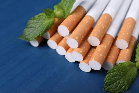Menthol cigarettes and mint leaves on blue wooden table, closeup. Space for t Stock Photos