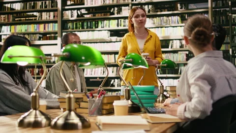 Mentor at group study speaking with peers seated at library table Stock Footage 336358331