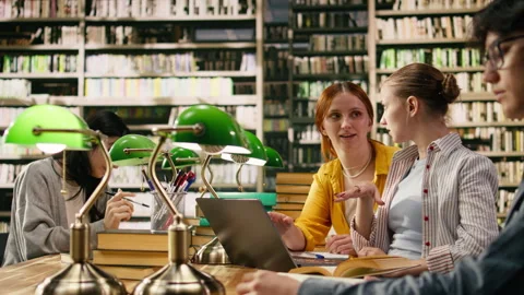 Mentor guiding student through academic work on laptop at library table Stock Footage 336358822