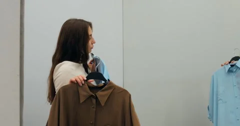 Merchandiser evaluating brown and blue tops choosing best combination of clothes Stock Footage 314466937