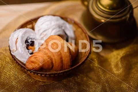 Meringue and croissant in a basket, next to a kettle Stock Photos