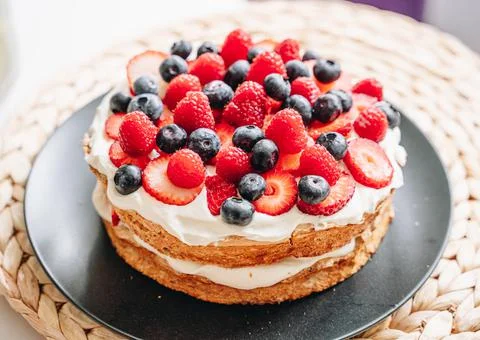 Meringue cake with fresh forest berries and cream on black plate Stock Photos