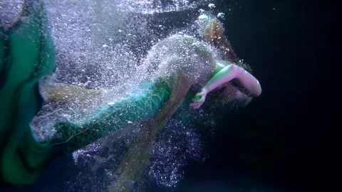A mermaid swims away into the dark abyss in streams of bubbles. view from the Видео 194422053